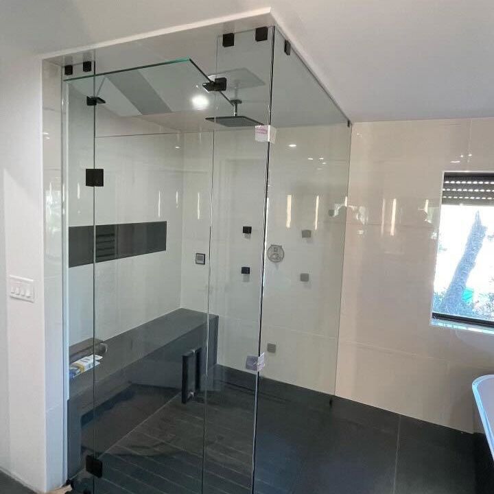 Frameless glass shower enclosure with a glass ceiling panel and matte black clamps, fitted under a sloped ceiling