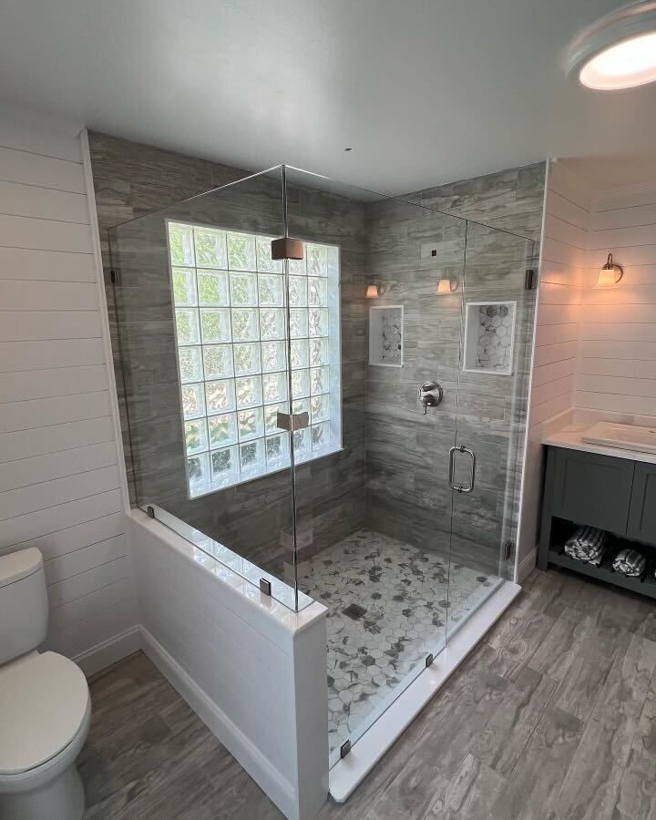 The same glass block window shower seen from the doorway, its frameless enclosure set against shiplap walls and a grey vanity