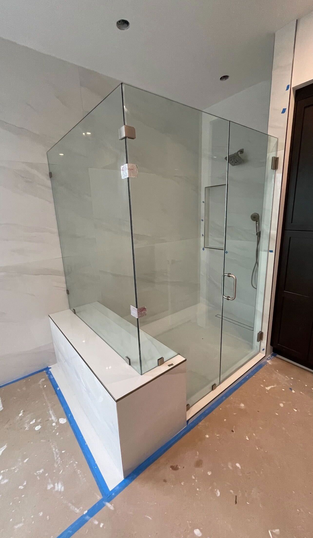 Frameless glass shower enclosure newly fitted, the panels still carrying their protective film and the floor still masked off