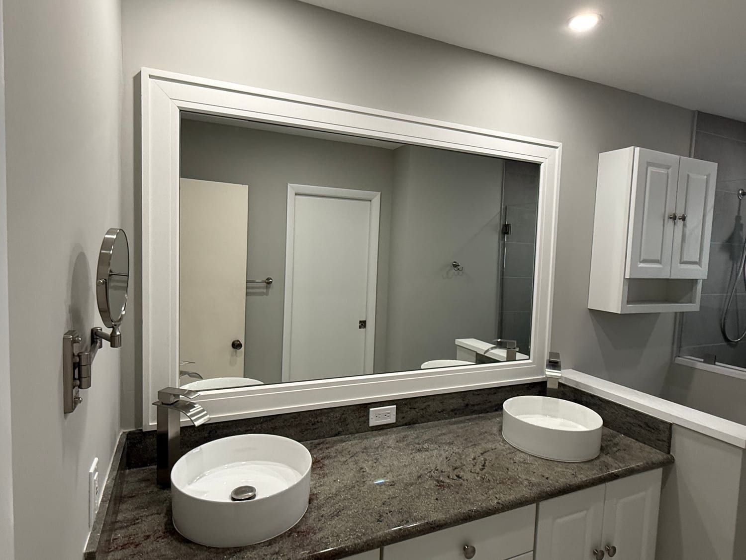 Wide mirror in a white painted frame above a granite-topped vanity with two white vessel basins