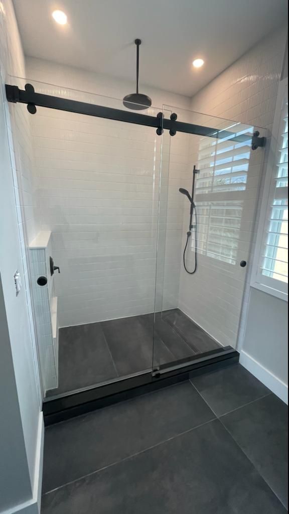 Sliding glass shower door on a matte black top track, with white tile walls and a dark tiled shower floor