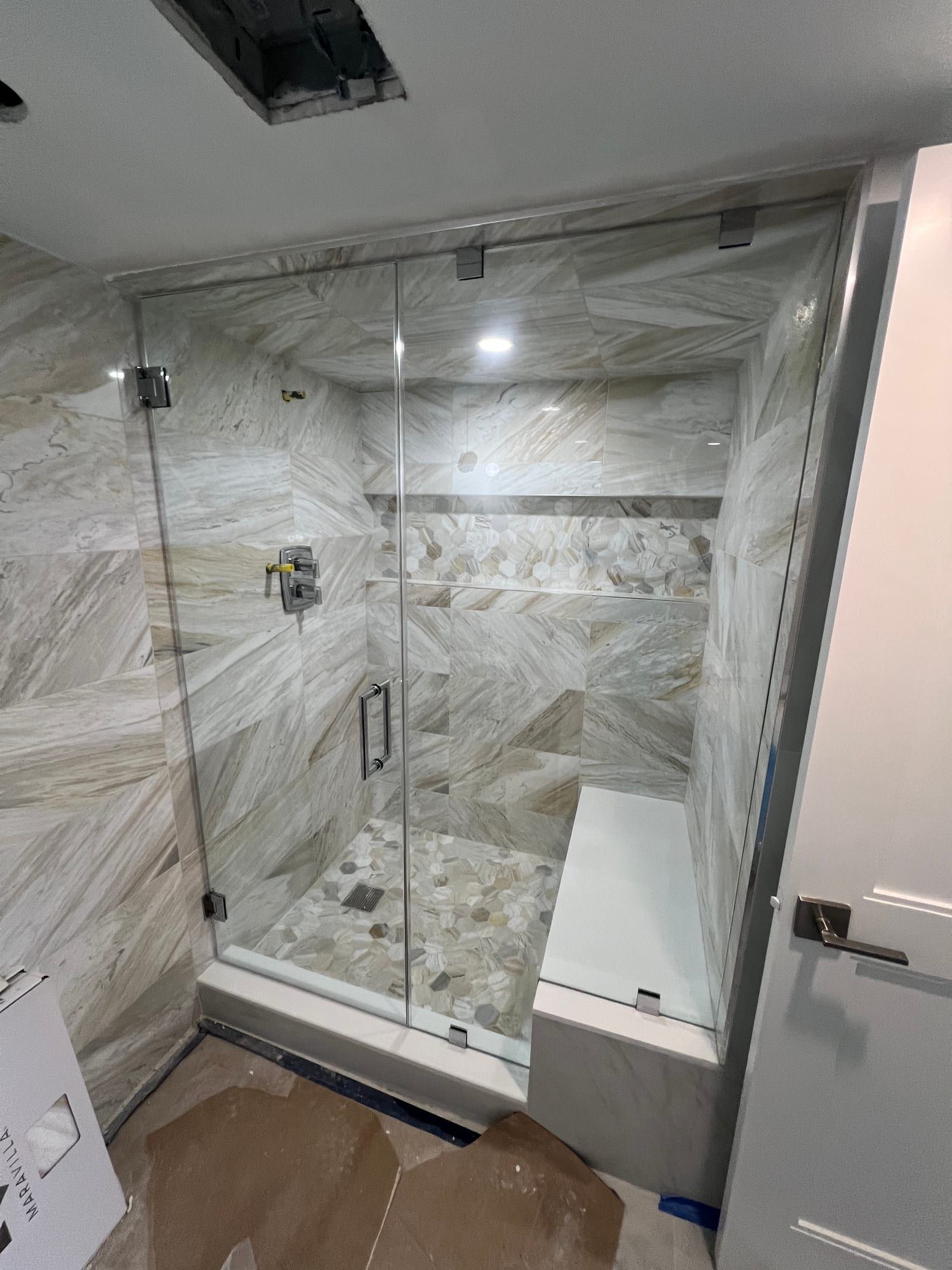 Steam shower enclosure with frameless glass carried to the ceiling on polished chrome clamps, a chrome ladder pull, marble-look walls, a hexagon mosaic floor and a built-in bench